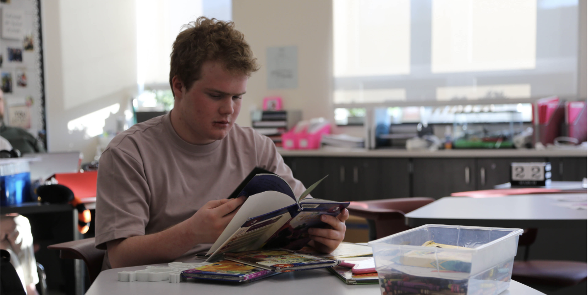 Reading away: Freshman and member of Conestoga’s Best Buddies chapter Sam Porter makes his way through the pile of books on his desk in special education teachers Madison Galanti and Jena Lutschaunig’s class. Porter said that he enjoys hanging out with other Best Buddies members.
